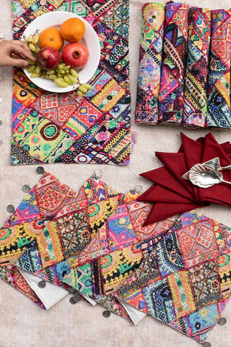 Colorful patterned placemats and napkins on a table with a person arranging fruit.
